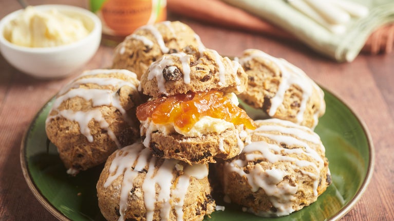 A pile of carrot cake scones on a green plate. The central scone has been cut in half with marmalade in the centre. In the background sits a jar of the marmalade with a used knife on top.